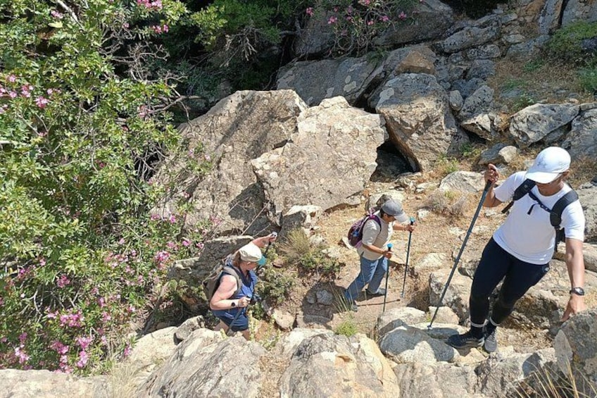 Hikers on a rocky trail with large boulders and some vegetation. 2