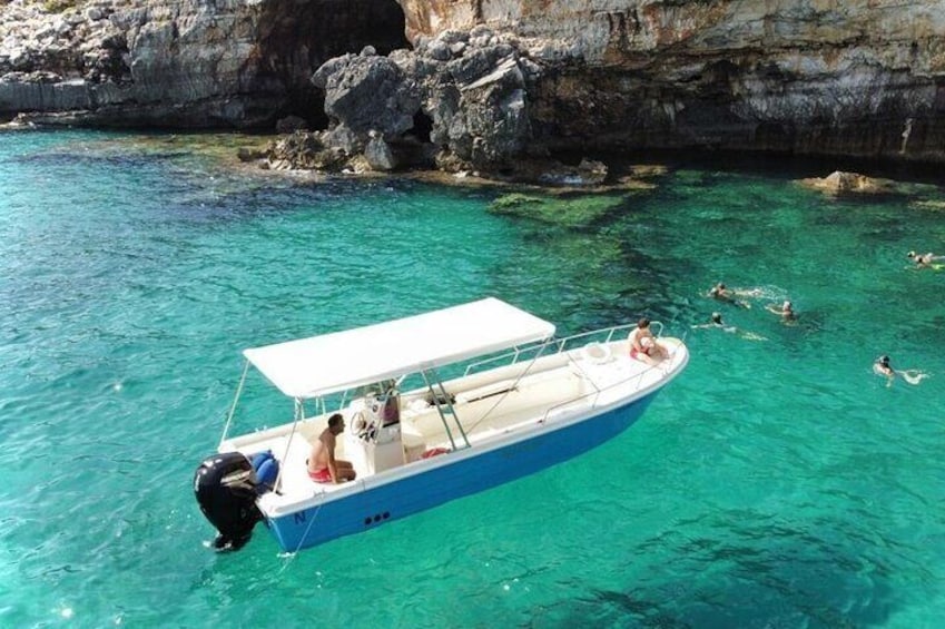 Un bateau se trouve dans l’eau, près de falaises rocheuses, et des personnes y nagent. 2