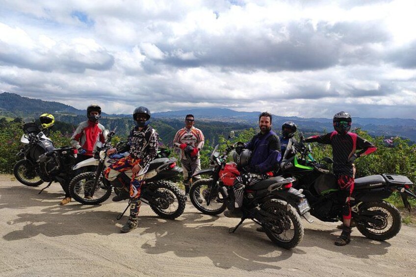 Eine Gruppe Motorradfahrer auf einem Feldweg, im Hintergrund eine gebirgige Landschaft. 3