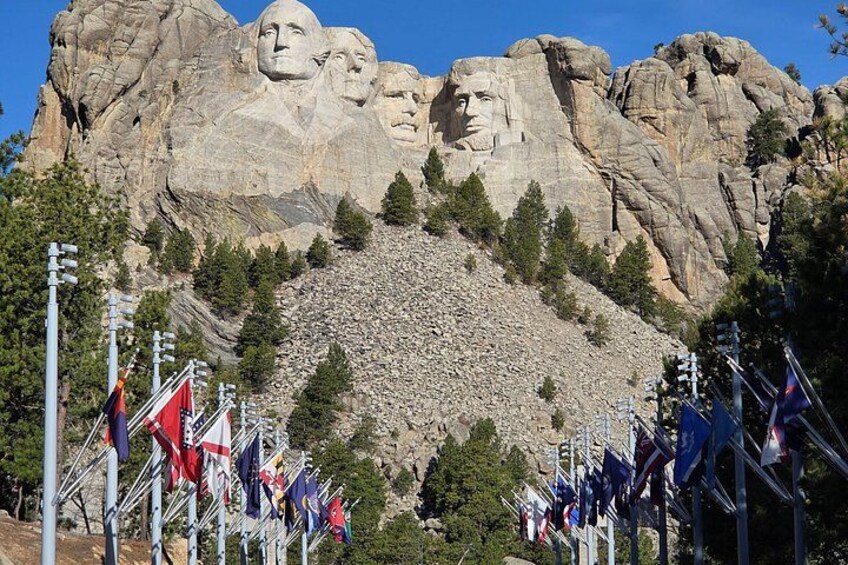 Mount Rushmore with four presidential faces, surrounded by trees and flags. 3