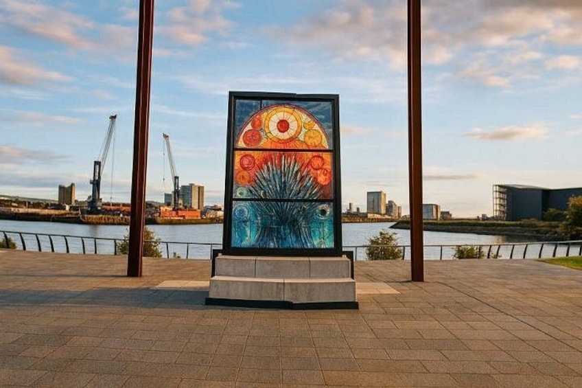 A colorful abstract sculpture in an urban setting with a river and industrial buildings in the background. 3