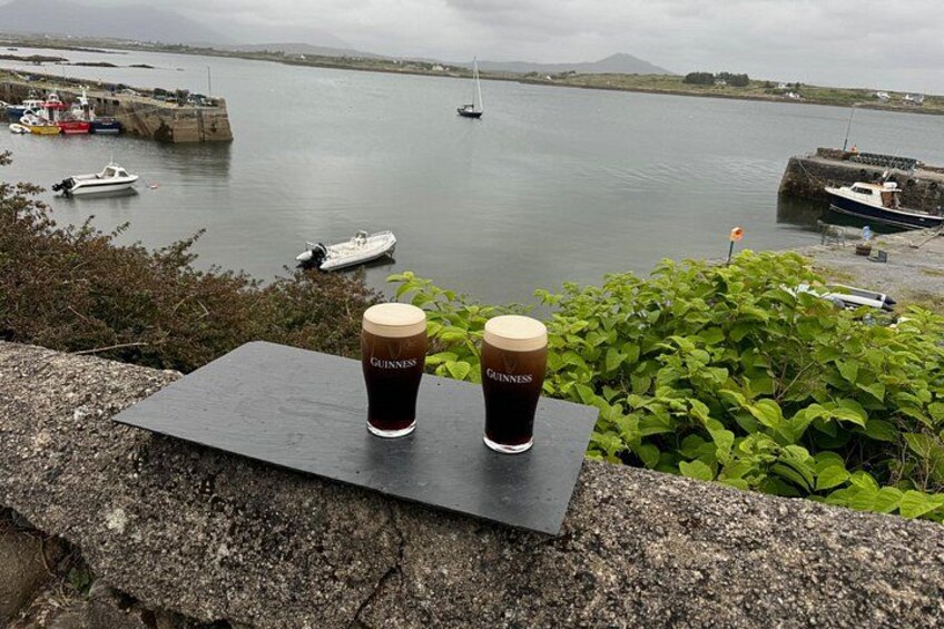 Deux verres de bière Guinness posés sur un rebord de pierre, donnant sur un port où sont amarrés des bateaux. 5