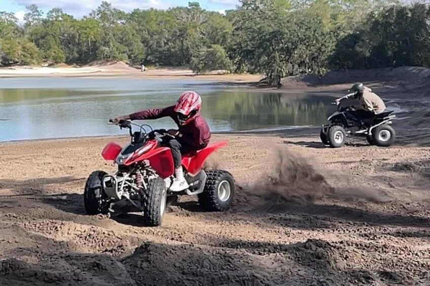 A person riding a red ATV on a dirt path near a body of water. 2