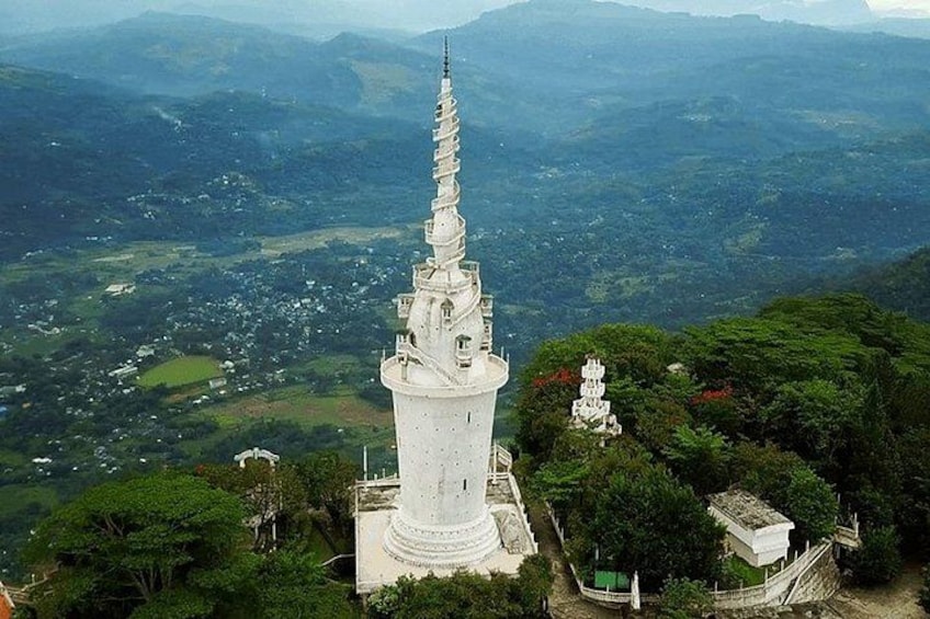 En hvid pagode med en spiraltrappe, omgivet af frodig vegetation og bjerge i baggrunden. 1