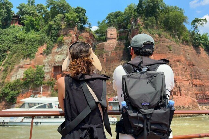 Dos personas con mochilas observando una gran estatua en un acantilado. 1
