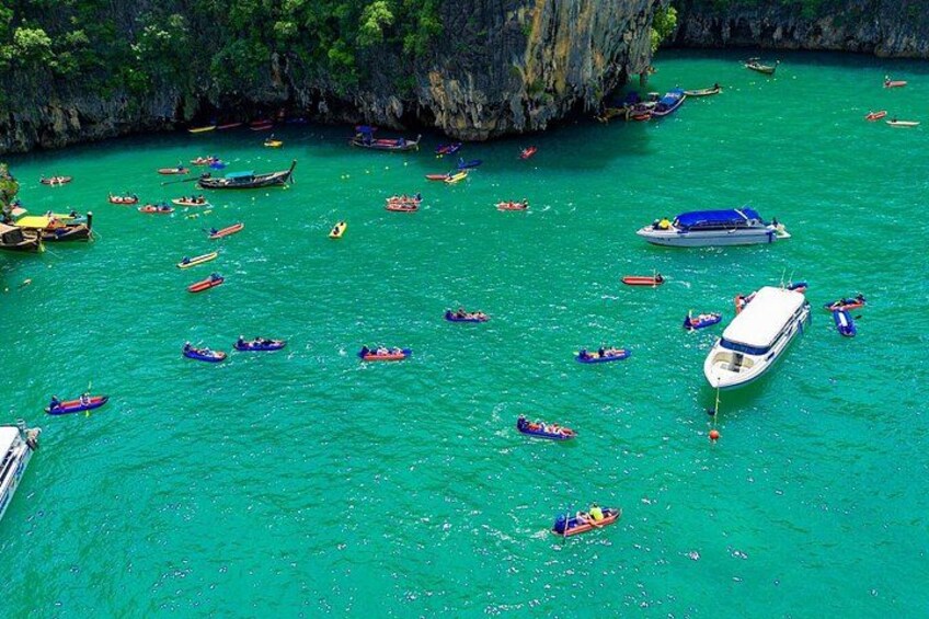 A turquoise sea with numerous boats, including motorboats and canoes, anchored or floating near a rocky cliff. 5