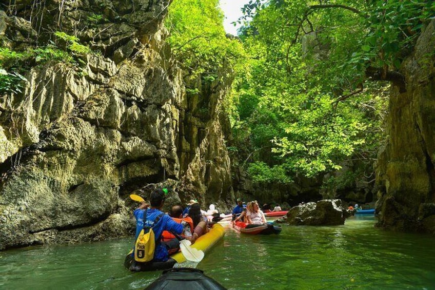 People kayaking in a narrow river surrounded by rocky cliffs and lush greenery. 1