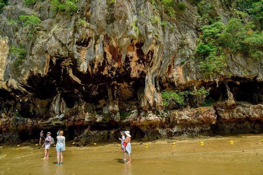 A rocky cliff with a cave entrance, a sandy beach, and people standing on the shore. 3