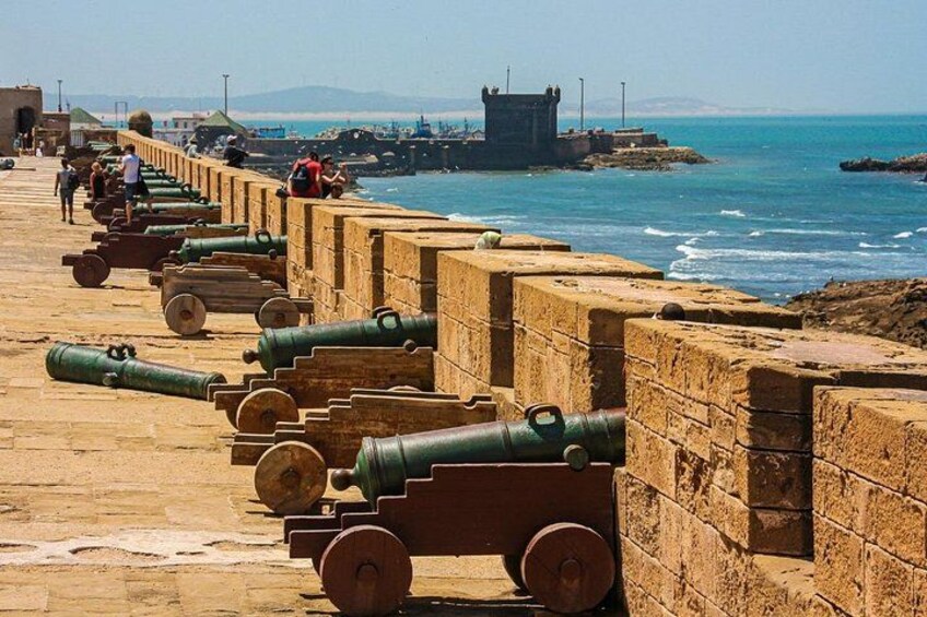 A coastal fortification with cannons lined up along a stone wall. 5