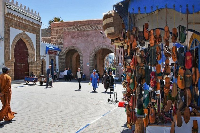 A market with a variety of shoes on display, a blue umbrella, and traditional architecture with arches. 2
