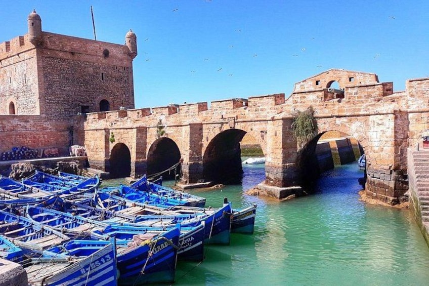 A historic stone bridge with arches, boats docked in a calm river, and a clear sky. 3