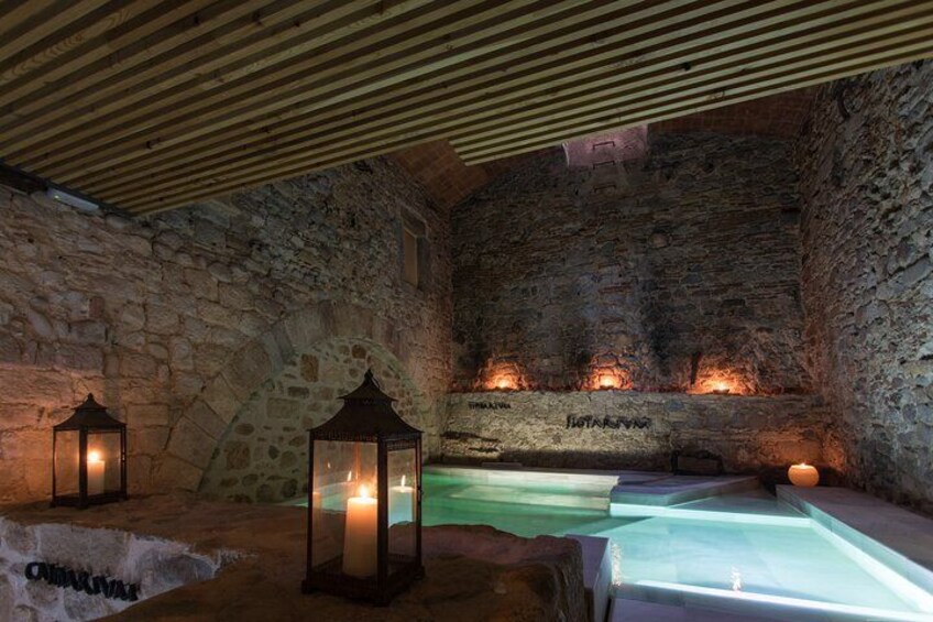 Ein Zimmer mit Steinwänden, einem Pool, Kerzen und Laternen. 3