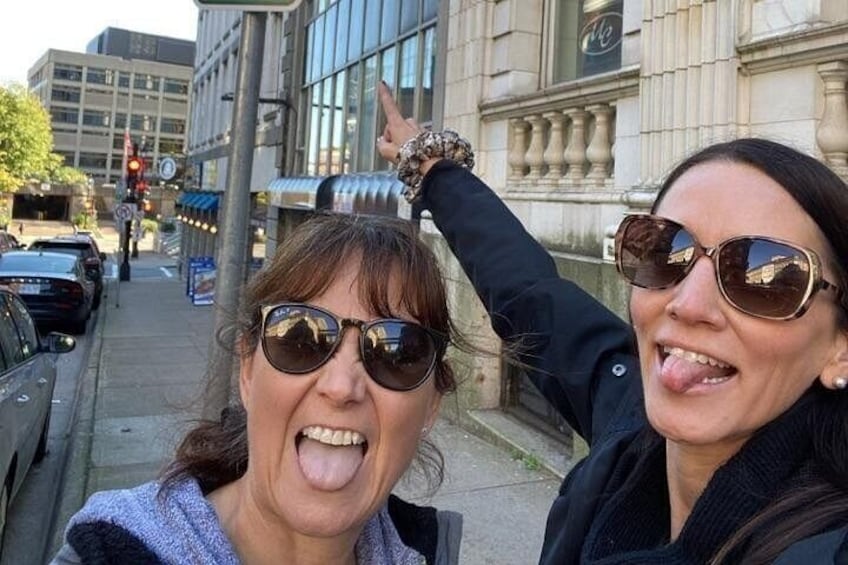Two people taking a selfie on a city street with buildings and parked cars in the background. 4
