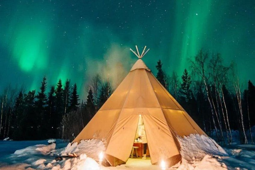 A snow-covered landscape with a lit tipi and aurora borealis in the background. 1