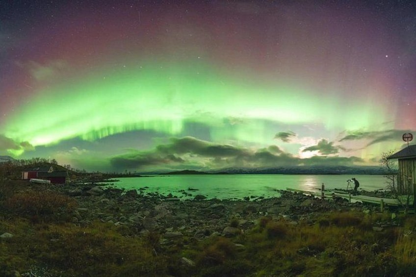 A night scene with the Northern Lights over a lake, a wooden structure, and a small building. 4
