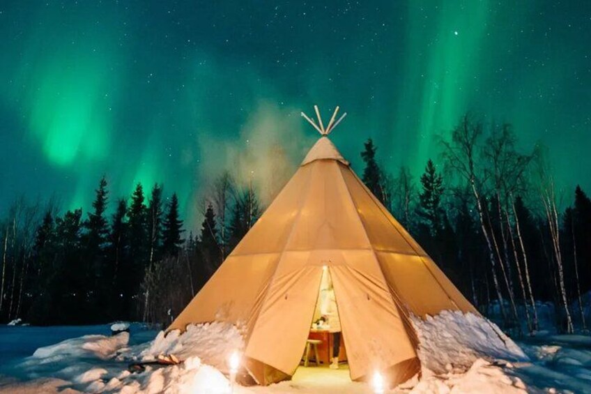 Et snedækket landskab med en oplyst tipi og nordlys i baggrunden. 1