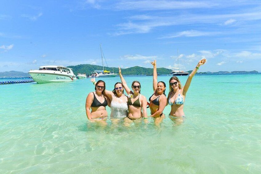 A group of people in a clear blue sea with boats in the background. 1