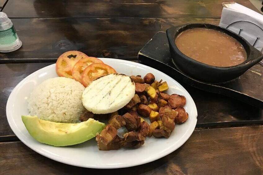 Een bord met rijst, avocado, gegrild vlees, gebakken plantains en een kom soep. 5