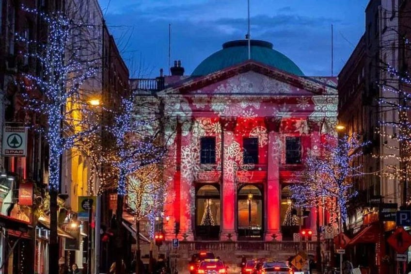 A building with classical architecture, illuminated by red and blue lights, surrounded by trees decorated with lights. 3