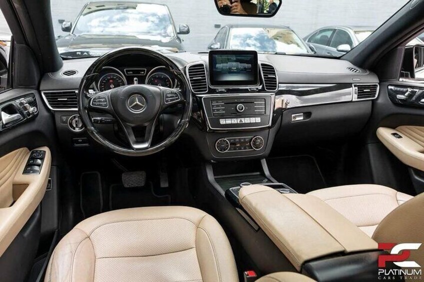 The interior of a Mercedes-Benz car with a steering wheel, dashboard, and beige leather seats. 3