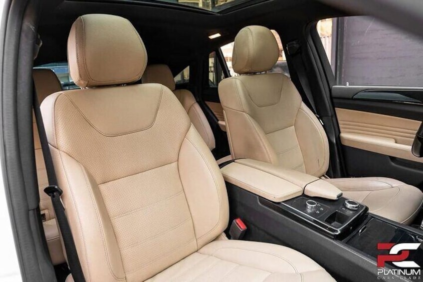 The interior of a car with beige leather seats and a center console with cup holders and a cup. 2