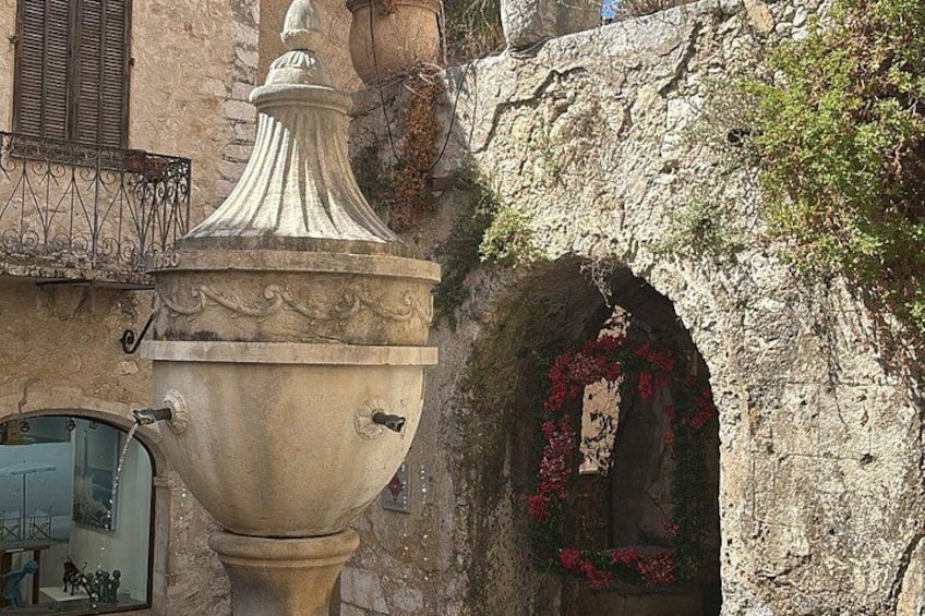 A stone archway with red flowers, a decorative urn, and a balcony with a wrought iron railing. 4