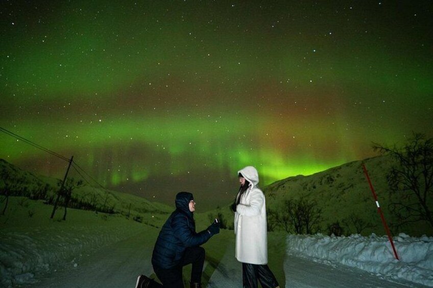 A person proposing to another under a green aurora display. 3