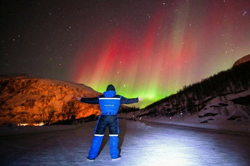 A person standing on a frozen surface, facing a vibrant aurora display. 2