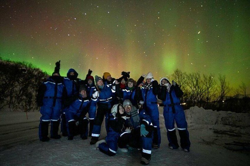 A group of people in blue winter gear posing under the aurora borealis. 4