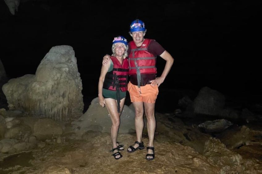 Zwei Personen mit Schwimmwesten und Helmen stehen auf felsigem Gelände vor großen Felsen. 2