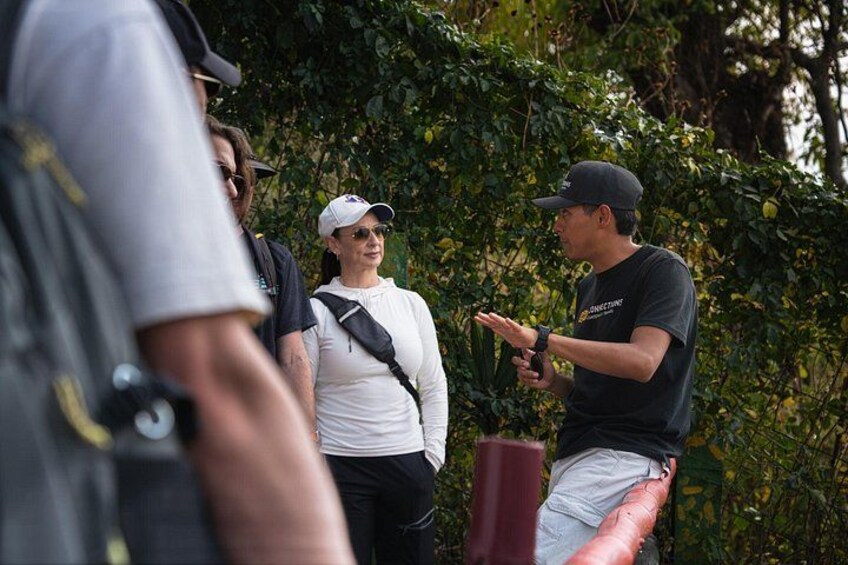 A group of people outdoors, one person gesturing while speaking, surrounded by greenery. 3