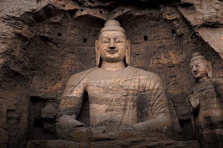 A large stone Buddha statue with intricate carvings and smaller Buddha figures in the background. 1