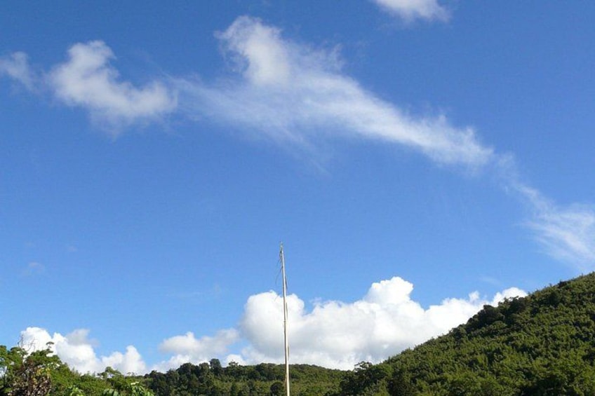 A clear blue sky with scattered clouds, a green hill, and a tall white pole. 3