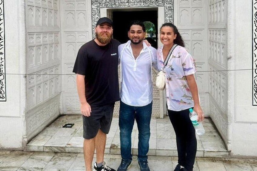 Three people standing in front of a building with intricate white carvings. 1