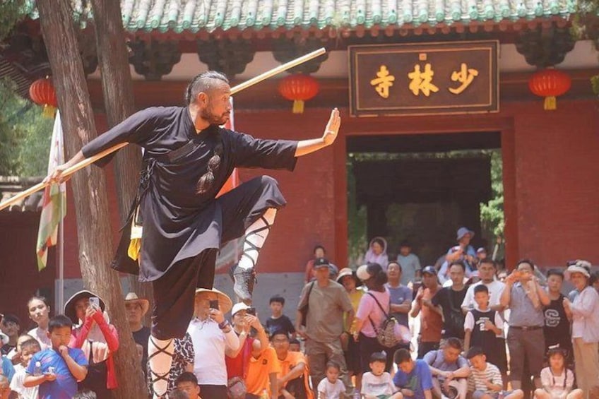 A person performing an acrobatic act with a pole, surrounded by a crowd. 4