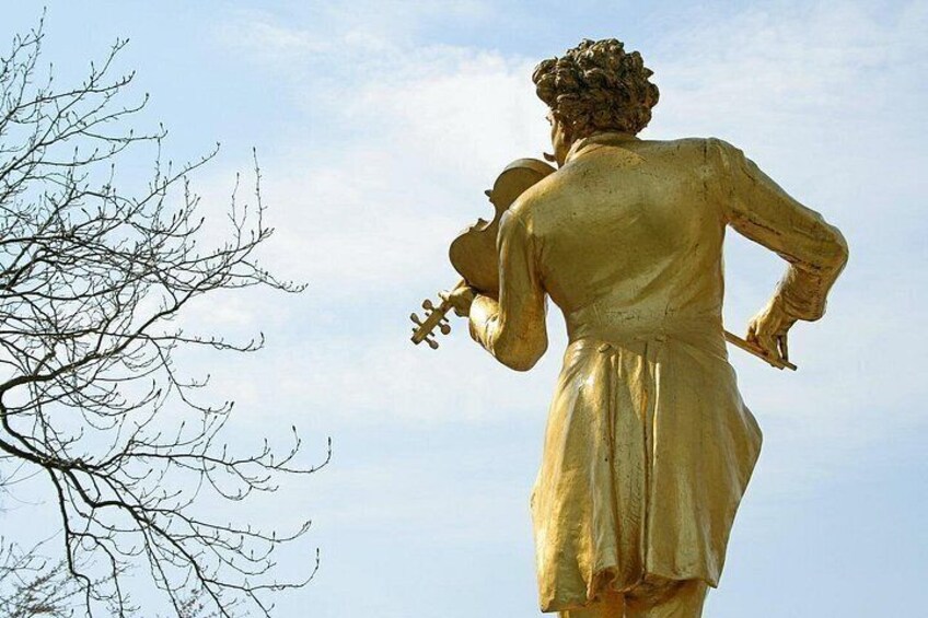 A golden statue of a man playing a violin, with a leafless tree to the left. 5