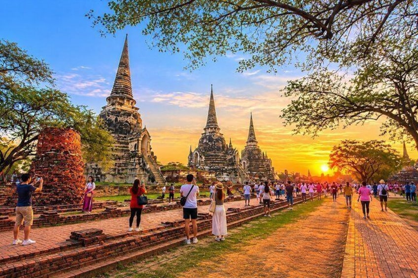 A temple complex with multiple spires, tourists walking along a pathway, and a sunset in the background. 1