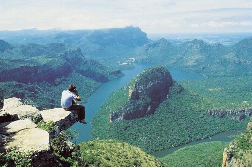 A person sitting on a rock overlooking a river valley with mountains in the background. 3