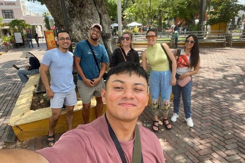 A group of people standing on a paved area with a tree and a yellow bench in the background. 4
