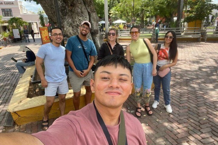 Un grupo de personas de pie en una plaza pública con un árbol y un banco amarillo. 4