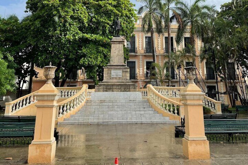 Un puente con una estatua en el centro, rodeado de palmeras y un edificio al fondo. 5