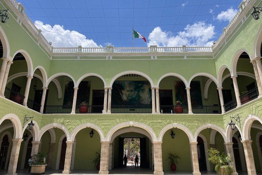 A courtyard with green arches, a flag, and a mural. 1