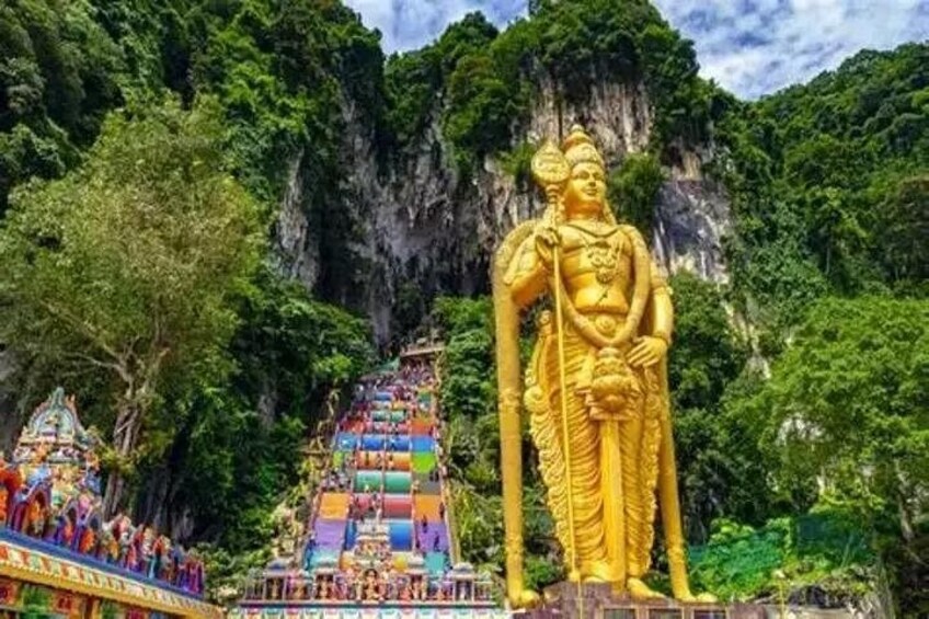 Un'imponente statua dorata in una zona montuosa, con un tempio colorato sullo sfondo. 1