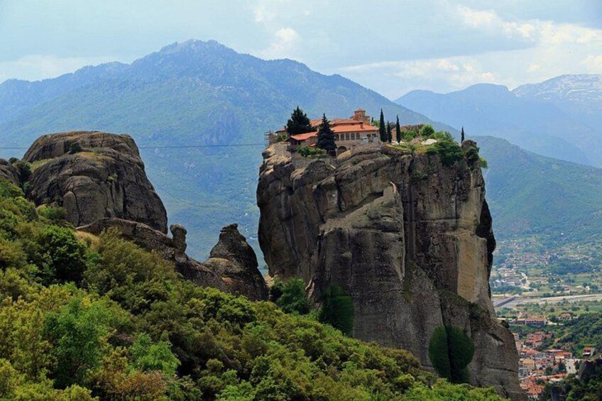 A monastery on a rocky cliff with a view of a valley and mountains in the background. 2
