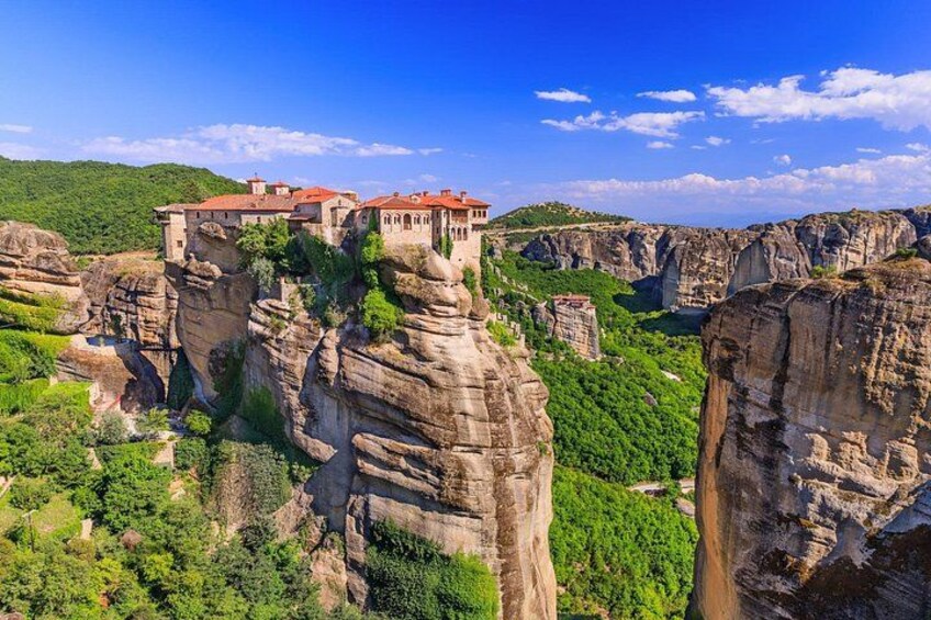 A monastery perched on a cliff with a lush valley below. 1