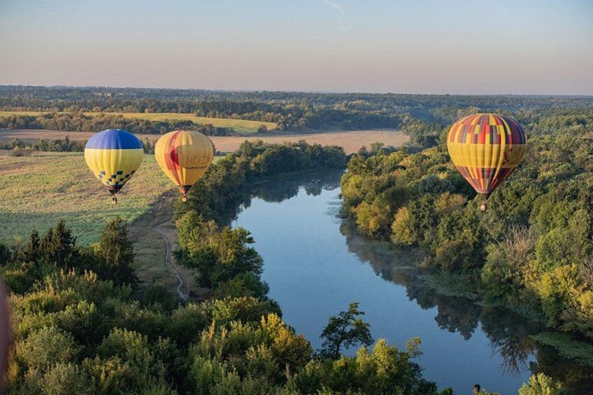Three hot air balloons over a river surrounded by trees. 1