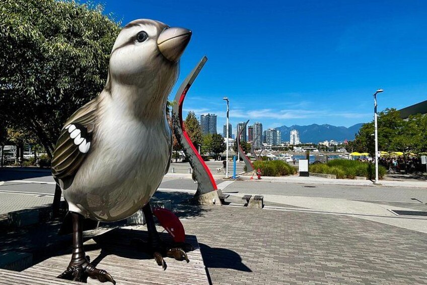 A large bird sculpture on a paved area with a cityscape in the background. 4