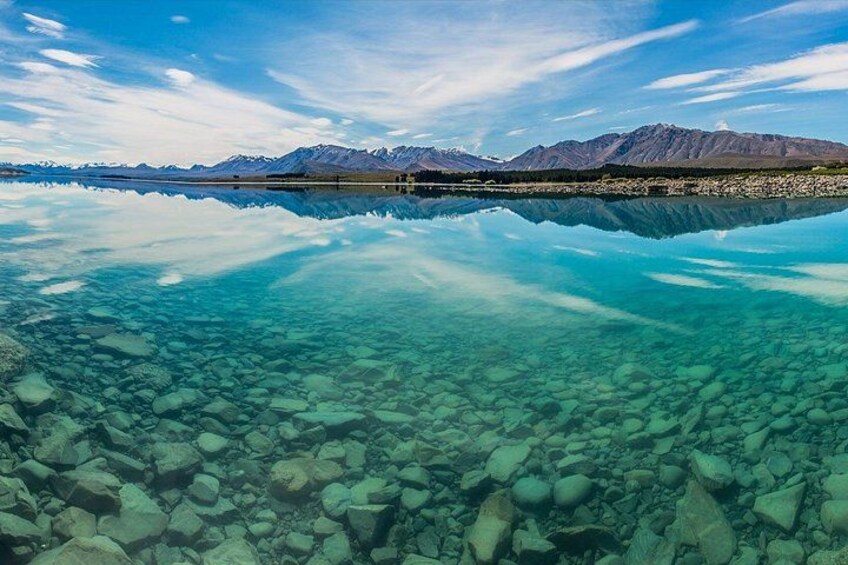 A clear lake with visible rocks and mountains in the background. 3