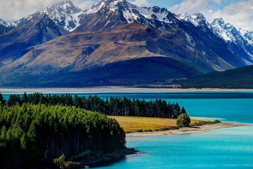 A mountain range with snow-capped peaks, a turquoise lake, and a dense forest. 1