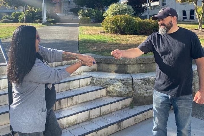 Two people shaking hands on outdoor steps with a grassy area and a building in the background. 3